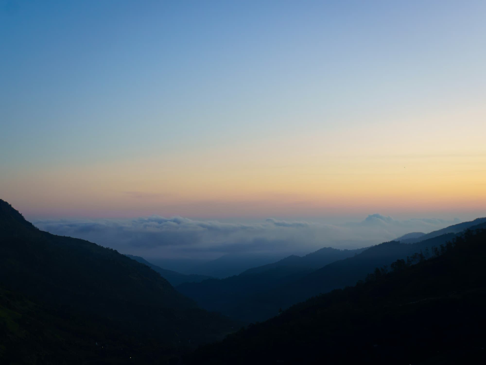 Layered hills at dawn beneath a soft pastel sky